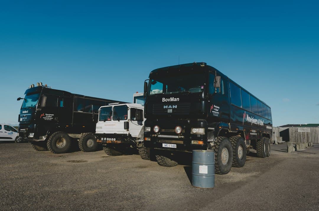 Three large black and white off-road tour trucks parked on a gravel lot — Photo by Aleksei Lebed on Unsplash