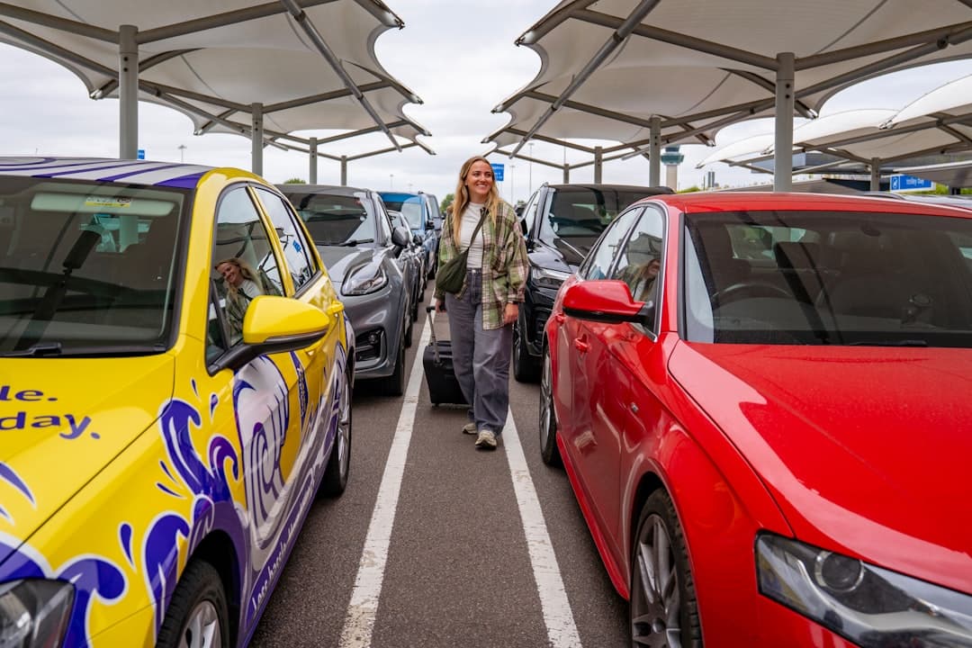 Woman with suitcase walking between parked cars. — Photo by Holiday Extras on Unsplash