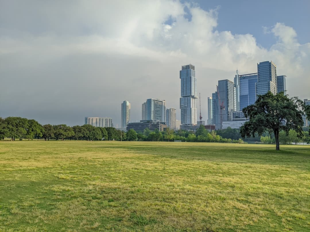 green grass field near city buildings under white clouds during daytime — Photo by Tomek Baginski on Unsplash