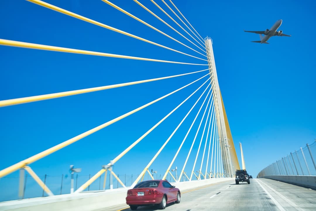 a red car driving across a bridge with a plane flying overhead — Photo by Yuriy Vinnicov on Unsplash