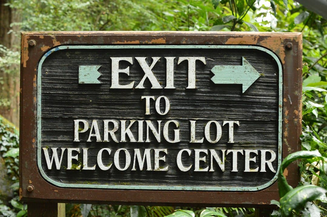 A weathered wooden sign reading EXIT TO PARKING LOT WELCOME CENTER in a forest — Photo by Naturalist Boat on Unsplash