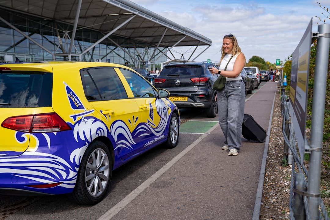 Woman with suitcase walks by a yellow taxi at airport. — Photo by Holiday Extras on Unsplash
