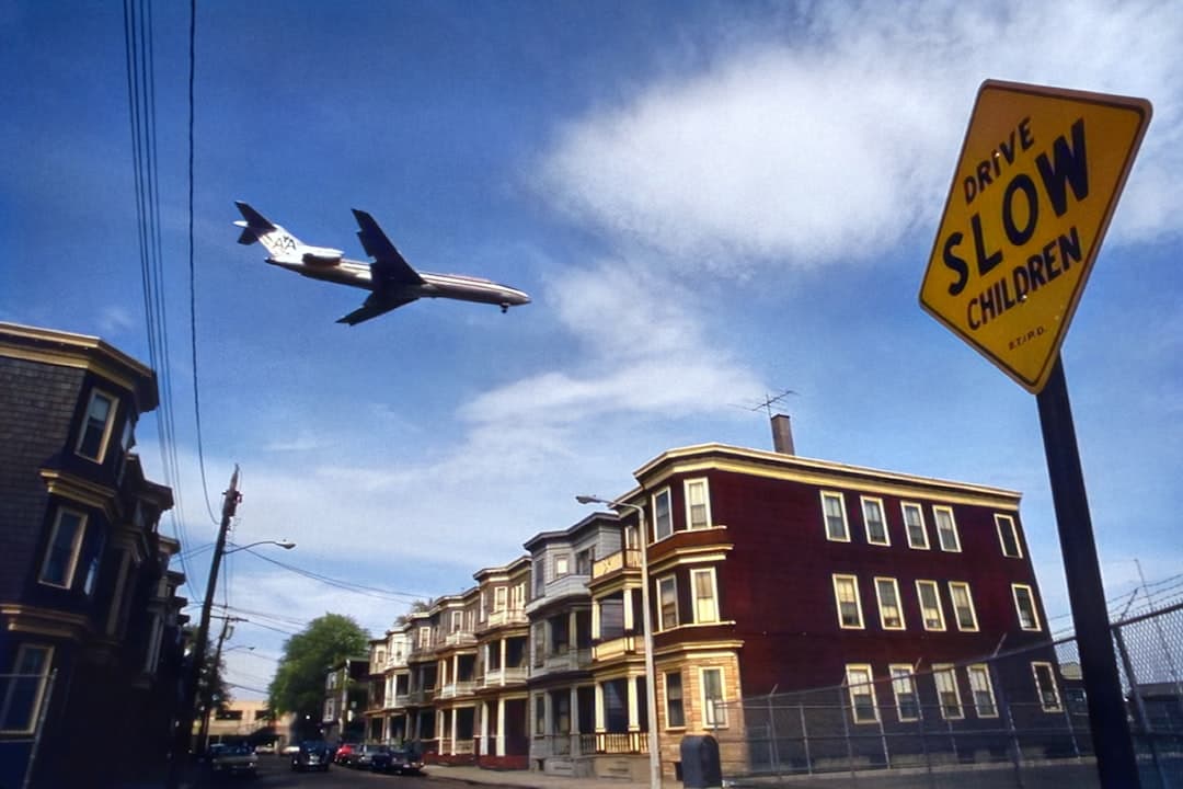 a plane is flying over a row of houses — Photo by Documerica on Unsplash
