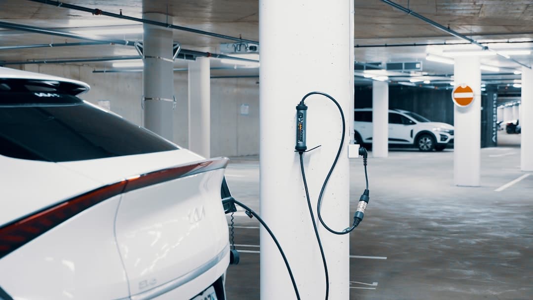 An electric car plugged into a pole in a parking garage — Photo by JUICE on Unsplash