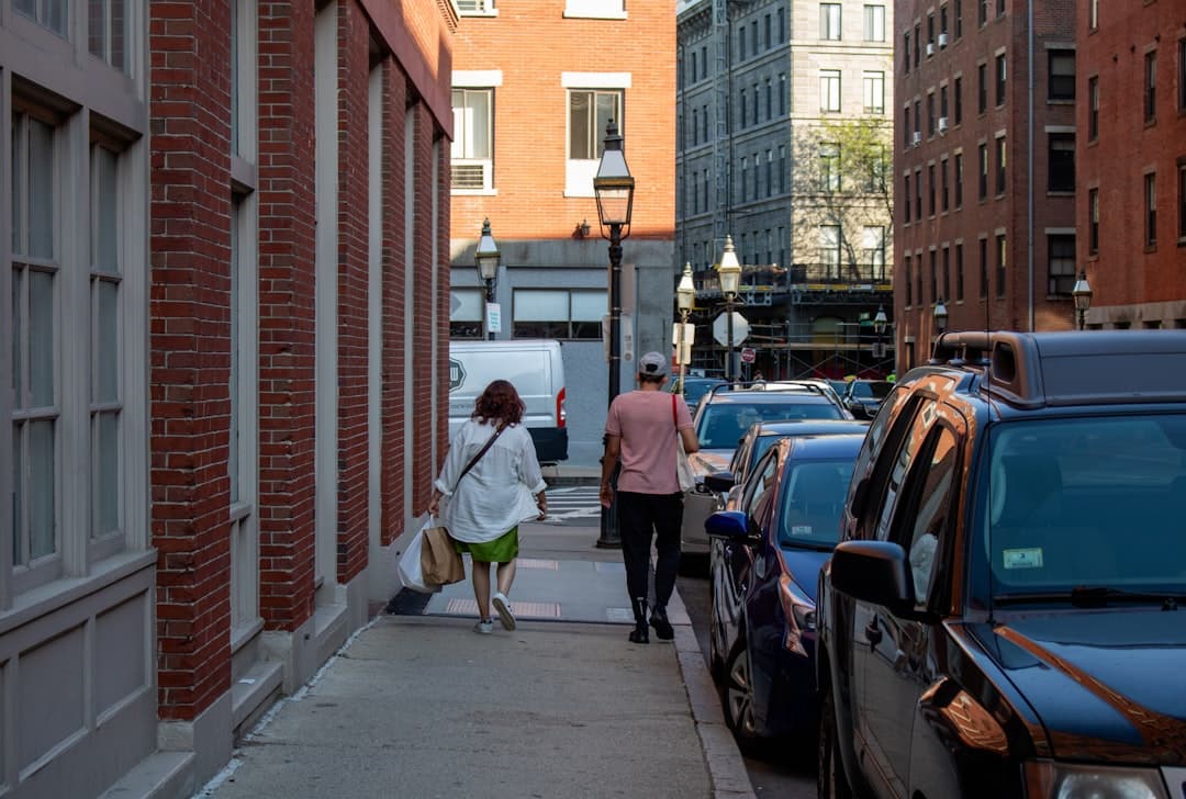 a couple of people walking down a sidewalk next to parked cars — Photo by Zoshua Colah on Unsplash