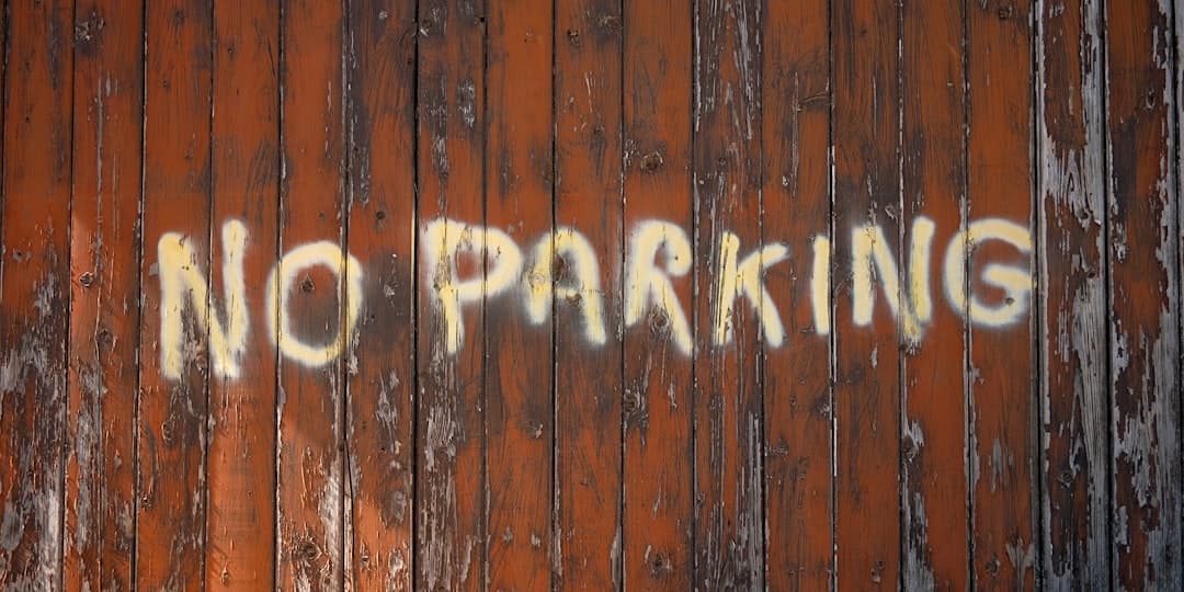 A no parking sign painted on a wooden fence — Photo by Marc Pell on Unsplash
