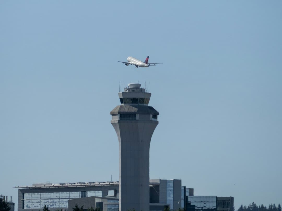 Commercial airplane ascending above an airport control tower — Photo by Justin McFadden on Unsplash